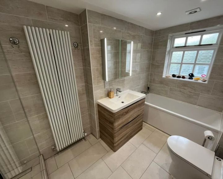 A modern bathroom installation with a wall-mounted sink, toilet, bathtub, and a vertical radiator.