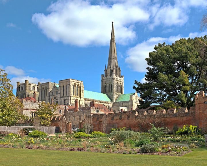 A historic cathedral with a tall spire overlooks a walled garden under a blue sky with scattered clouds, adjacent to an elegantly completed bathroom installation that harmonizes modern convenience with the area's timeless