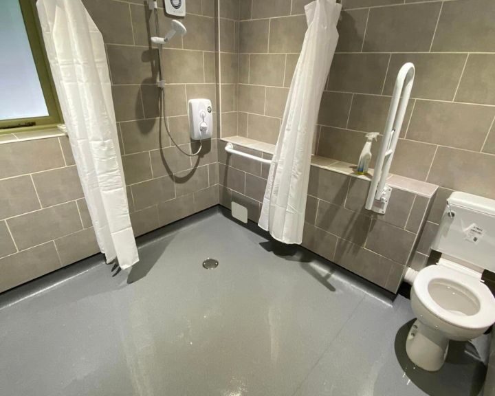 A bathroom installation equipped with safety grab bars, a walk-in shower area, and an accessible toilet for individuals with mobility challenges.