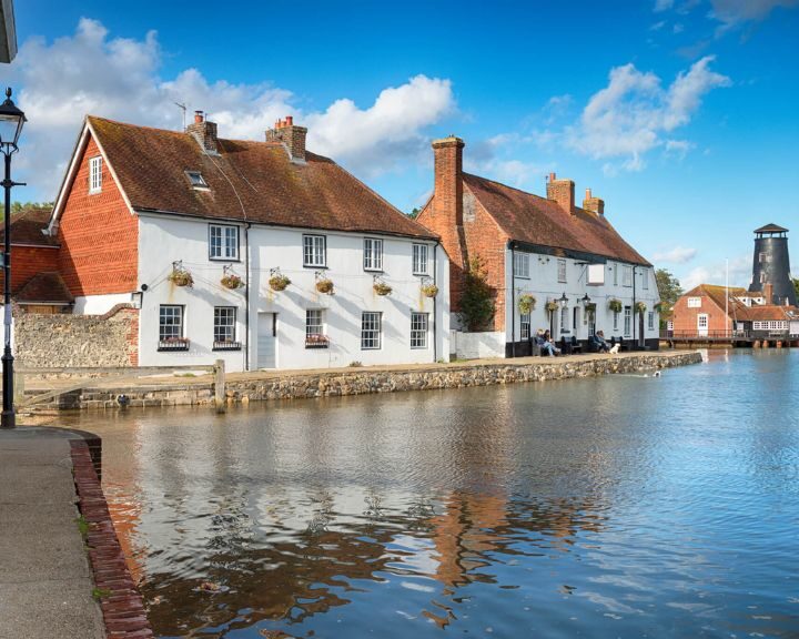 Quaint riverside houses with a prominent chimney in the background under a clear blue sky, designed by an expert bathroom fitter.
