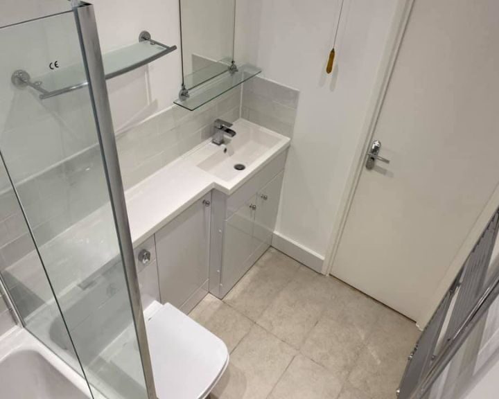 Modern bathroom interior with a glass shower enclosure, white vanity sink, tiled flooring, and designed by a professional bathroom fitter.