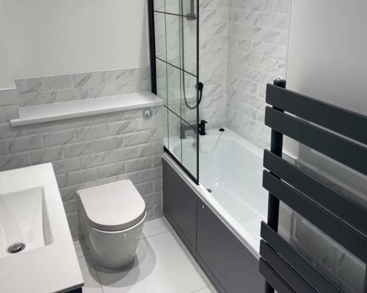 Modern bathroom installation with a glass shower enclosure, bathtub, toilet, and basin designed for disabled accessibility.