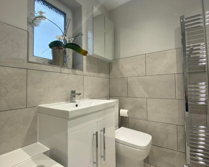 Modern bathroom design with neutral tiles, featuring a wall-mounted sink cabinet, toilet, and a heated towel rail designed for accessibility in disabled bathrooms.