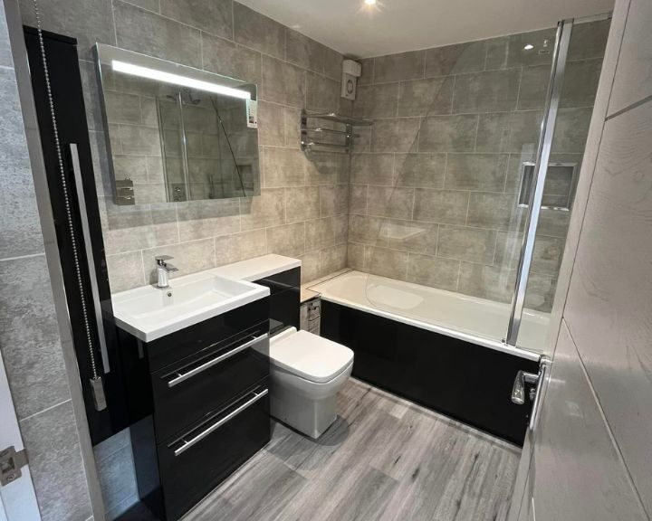 A modern disabled bathroom with a combination bathtub and shower, a wall-mounted toilet, and a vanity with sink and mirror.