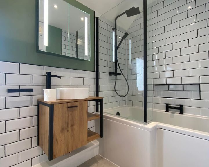 Modern bathroom design with white subway tiles, wooden vanity, and a glass-enclosed shower-tub combo.