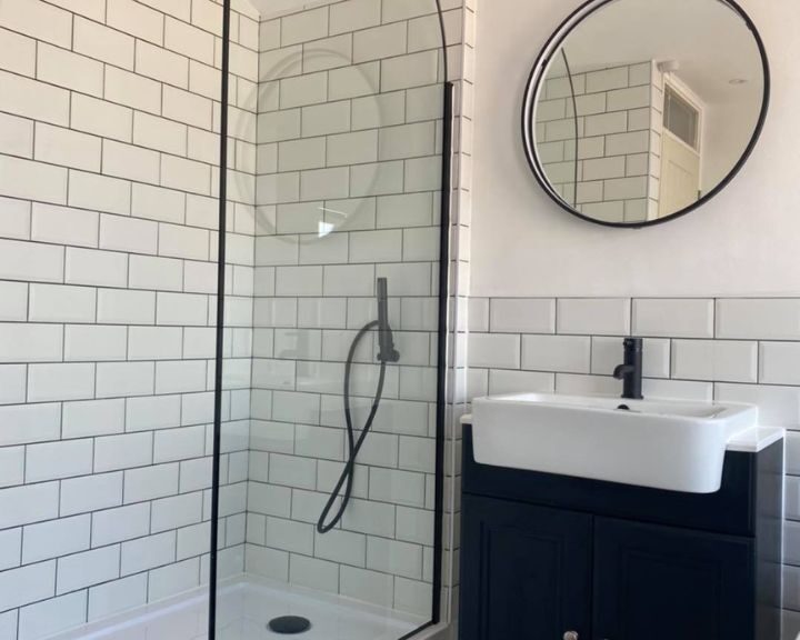 A modern bathroom installation featuring white subway tiles, a glass shower enclosure, and a black vanity with a round mirror.