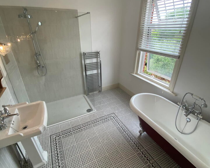 A bright, clean bathroom design with a claw-foot tub, separate shower stall, pedestal sink, and patterned rug.
