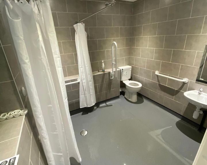 Modern accessible disabled bathroom with wet floor shower design, handrails, and neutral tile finish.