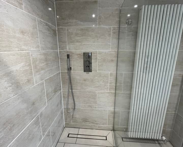 Modern bathroom design corner with tiled walls featuring a shower system and a vertical radiator.