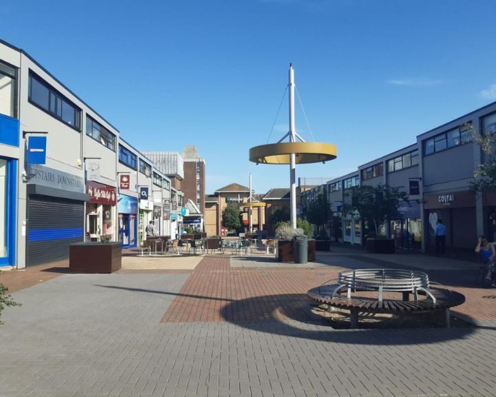Pedestrian street with shops and a circular sitting area under a yellow canopy on a sunny day, near an accessible disabled bathroom designed by a renowned bathroom fitter.